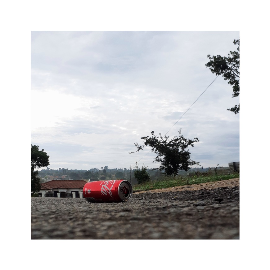 A low perspective photo of a can of soda lying on the side of the road.