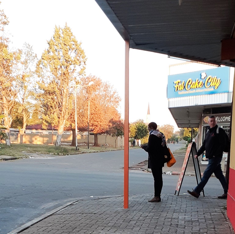A woman busy on her phone. A man is walking past her and looking into a shop.