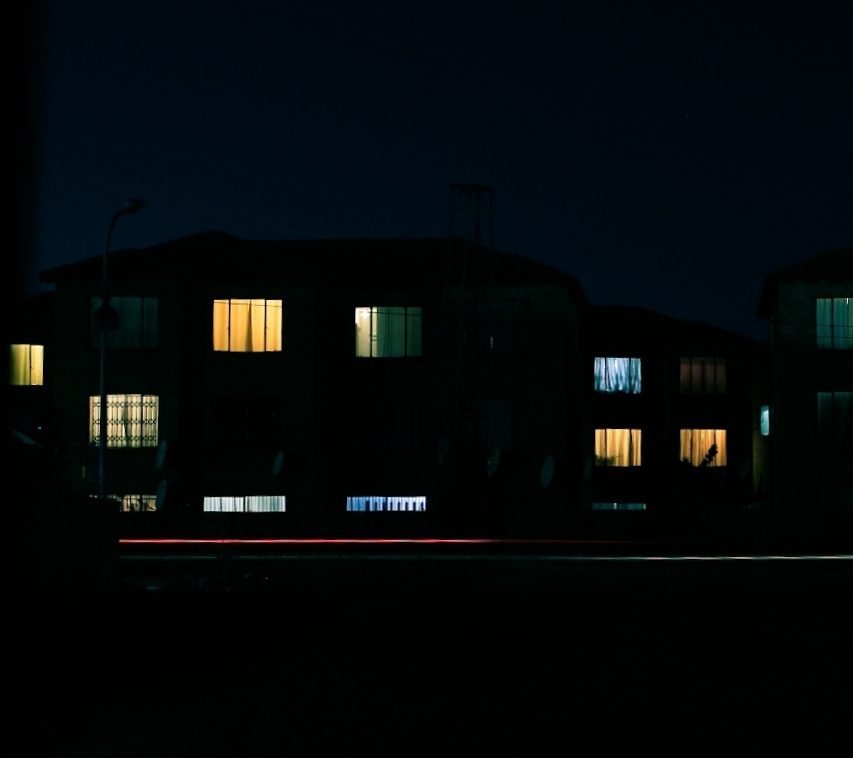 An apartment block with lights on in the windows. In the front a long exposure light trail.