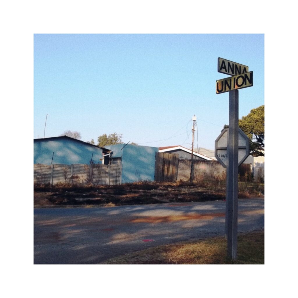 A light blue house. In the foreground a sign indicating the two names of the streets.
