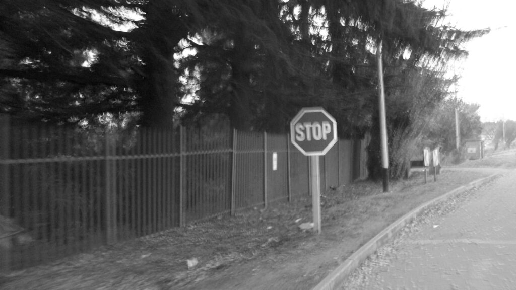 A traffic sign captured in front of a palisade fence. Photo in black and white.