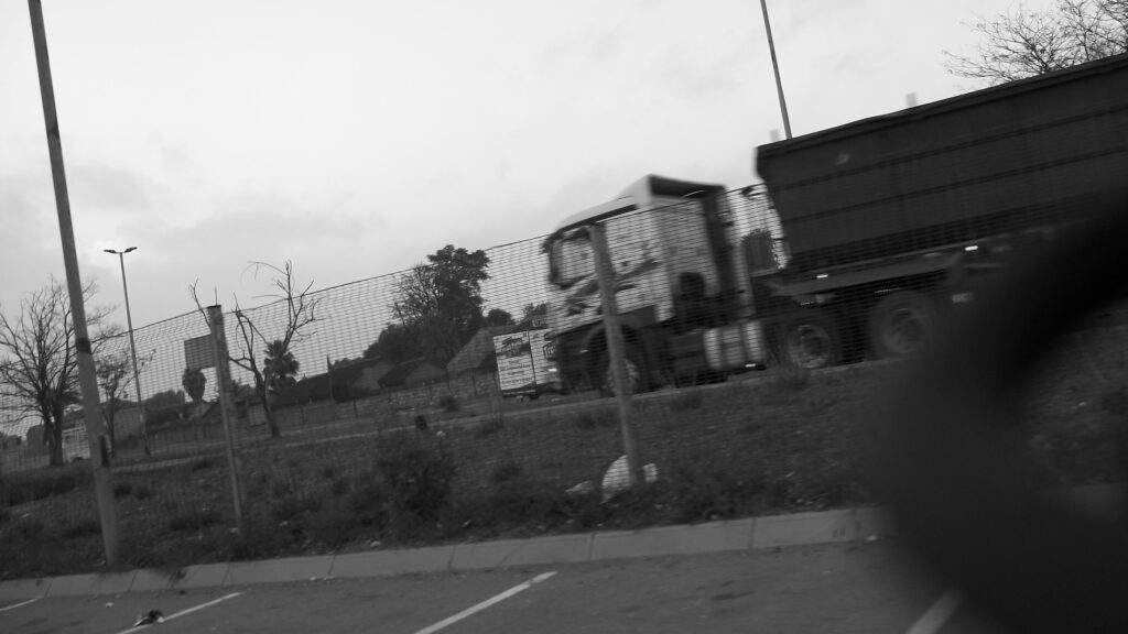 A photo of a truck driving past a fence. The truck is slight blurred and out of focus.
