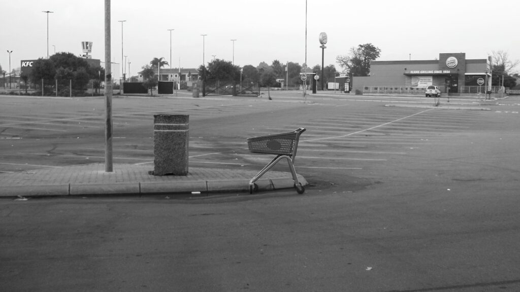 A shopping cart, or trolley as we call them standing in an empty parking lot.