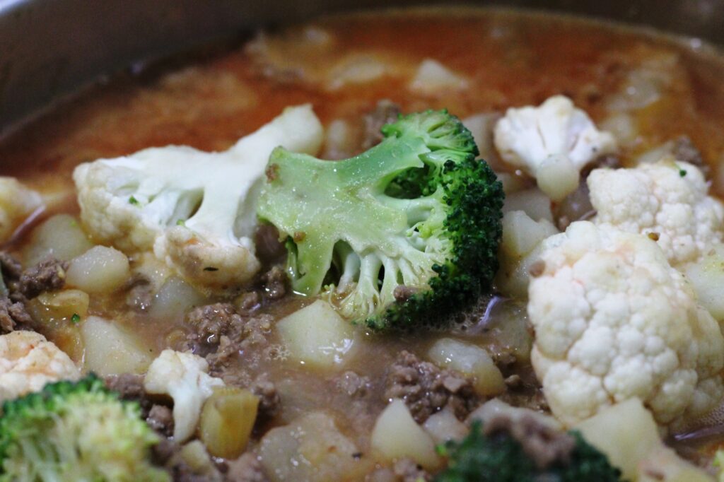 Broccoli in a pan along with cauliflower and ground beef.